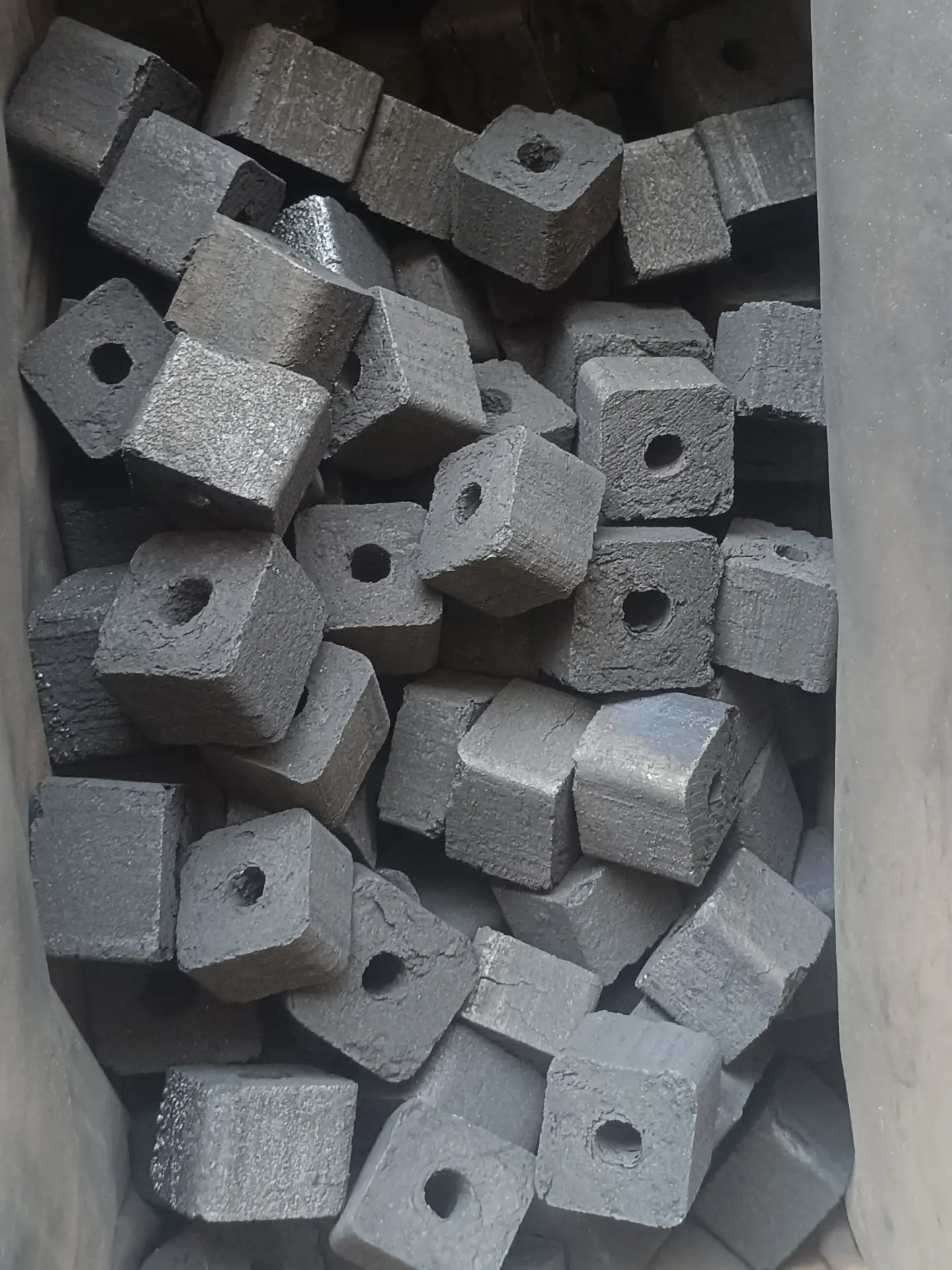 Small cube-shaped shisha charcoal pieces, each with a center hole, in a production basket