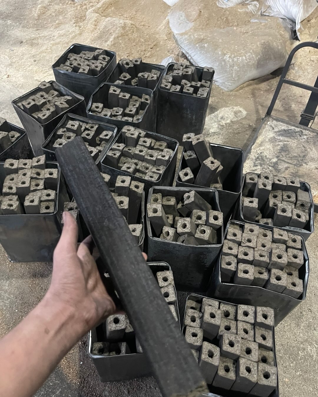 Cube-shaped shisha charcoal in production molds, hand holding a piece